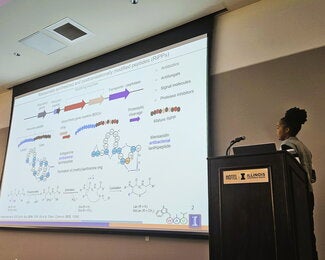 Student standing at a podium presenting research on a large overhead screen.