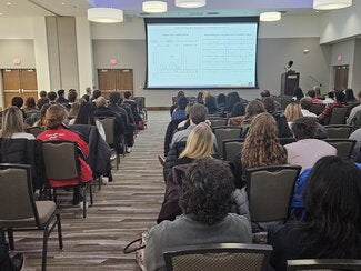 Large conference room filled with people in chairs listening to a presentation