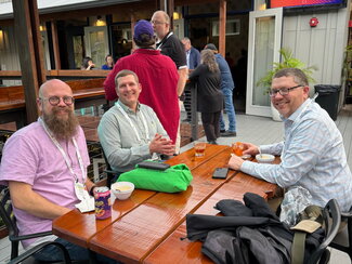 Three event attendees sitting in chairs at a table in an outdoor venue