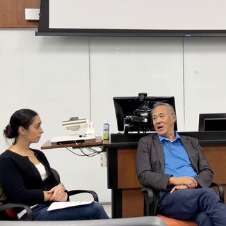 Prof. Tasha Manesis (seated in chair) listens to Alan Wu (also seated) answer a panel question.