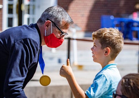 Martin Burke with his medallion hanging from his neck as he bends over talking to his son during the Presidential Medallion ceremony. 