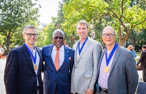 Martin Burke with medallion around his neck stands next to Chancellor Robert Jones, who's next to Paul Hergenrother with his medal around his neck and vet med professor Timothy Fan with his medal around his neck. They are standing together on the quad on the UIUC campus.