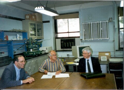 A photo of Iain Paul, center, sitting with two colleagues at a large table in his lab.