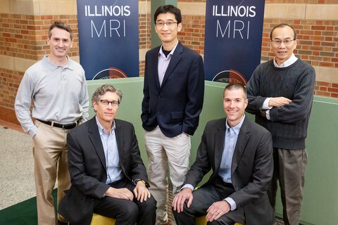 Researchers pose, some standing and some sitting, together in front of two blue MRI banners.