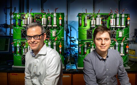 Portraits of Martin Burk and Daniel Blair, each sitting in front of the automated machine they developed.