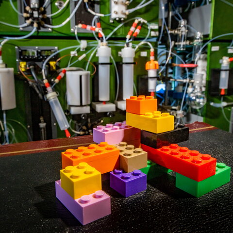 A photo of Lego blocks in the foreground and the automated molecule building machine in the background.