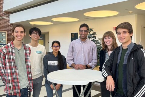 Undergraduate students and Stephen Kocheril stand around a small table in the atrium of CLSL.