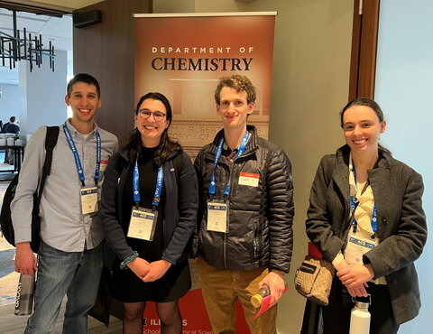 Four alumni stand side by side in front of a chemistry banner at the reception.