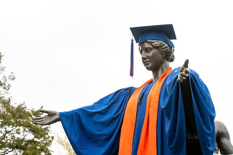 Photo of Alma Mater statue dressed in orange and blue graduation cap and gown.