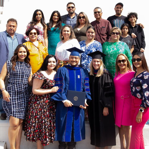 Daniel Najera in blue and orange graduation regalia with his family members and PhD advisor 