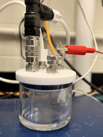 A glass jar holding plasma solution sits on a table with electrical wires and other items connected to it.