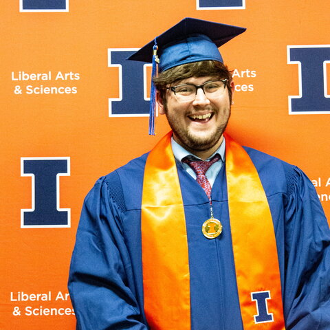 Ian Garvey in a cap and gown standing in front of an orange background