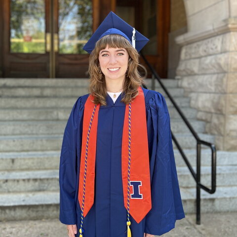 Portrait of Megan Murphy in graduation regalia standing in front of Noyes entrance