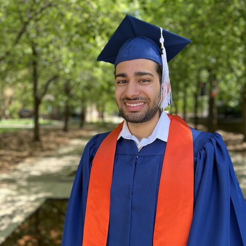 Qasim Sikander in cap and gown outdoors on the UIUC campus with trees in background