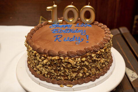 Picture of a chocolate-iced cake on a table with 100 on the top.
