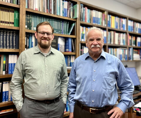 Ian Rinehart and Scott Denmark stand side by side in front of a bookshelf lined wall.