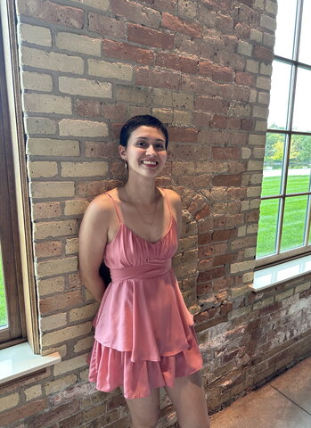 Jazmin stands in front of a brick wall between two large windows inside a building
