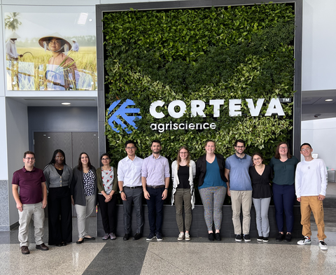 Graduate students stand side by side in front of a Corteva sign at the Corteva facility.