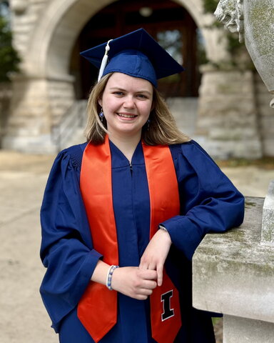 Olivia Nobbs in orange and blue graduation regalia leaning on a concrete statue in front of Noyes entrance.