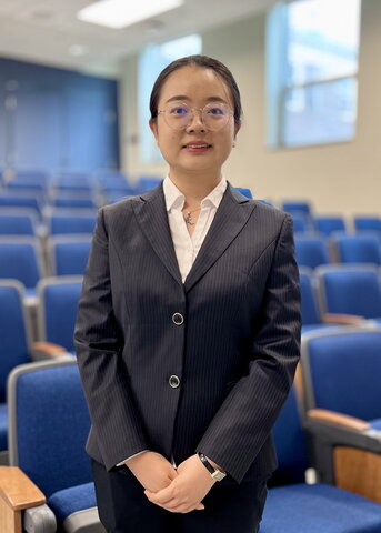 Portrait of Qi Hua standing in a lecture room with seats in the background 