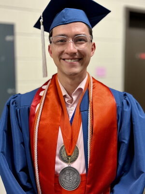 Student standing in graduation cap and gown with medals around his neck