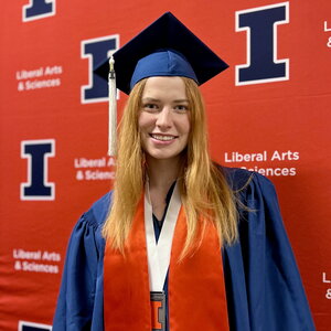 Student in a cap and gown standing in front of an orange background