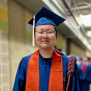 Student standing in a cap and gown in a hallway
