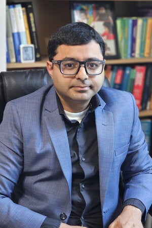 Portrait of Subha Mukherjee sitting in a chair in front of a book shelves