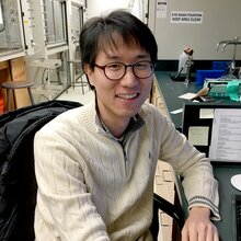 Portrait of research scientist Hong-Jun Cho sitting at a desk in a lab