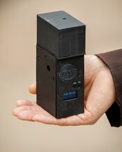 A closeup image of a small rectangular-shaped black box, a prototype of the spot device, sits in the palm of a human hand.