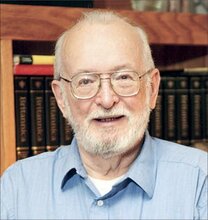 Head shot of the late Paul Lauterbur, in front of books on a shelf in a blue collared shirt.