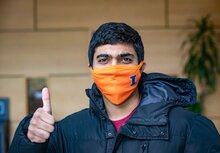 A UIUC student wearing an orange block I decorated COVID-19 mask is looking into the camera, giving a thumbs