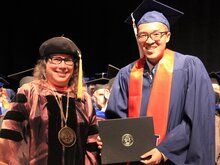 Cathy Murphy stands next to Ayman Roslend on stage during convocation.