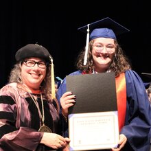 Cathy Murphy stands next to Claire Zimmerman on stage during convocation.
