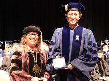 Cathy Murphy stands next to Kaibo Feng on stage during convocation.
