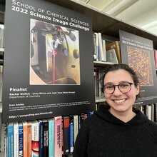 Rachel Wallick stands next to a poster of her science image hanging on a bookshelf in the chemistry library.