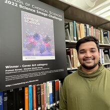 Prateek Bansal stands next to a poster of his science image hanging on a bookshelf in the chemistry library.