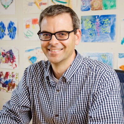 Portrait of Martin Burke seated with a white wall behind him that is full of colorful drawings