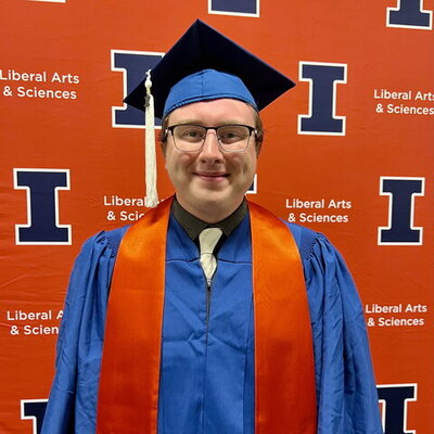 Zachary Burke in graduation regalia in front of an orange backdrop