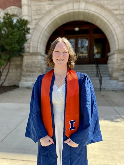 Makenna Pinkham in graduation robe standing in front of Noyes entrance