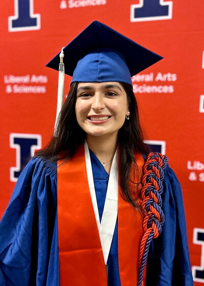 Student standing in a graduation cap and gown on an orange background