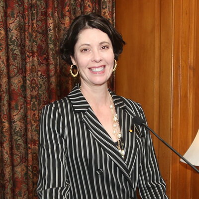 Portrait of Landes standing at a podium with a microphone in front of her