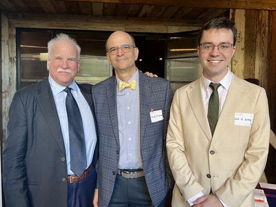 Three people in suits and ties standing side by side at a reception