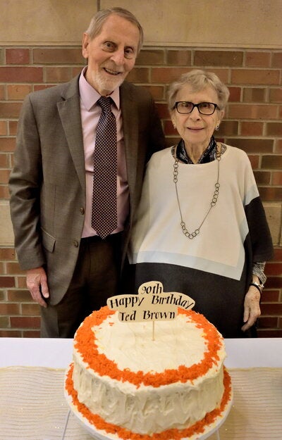 Two people standing together behind a table with a large birthday cake