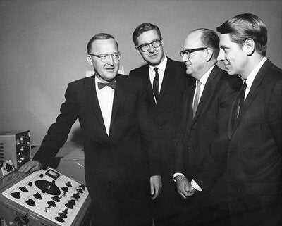 Black and white image of four men gathered around a piece of lab equipment 
