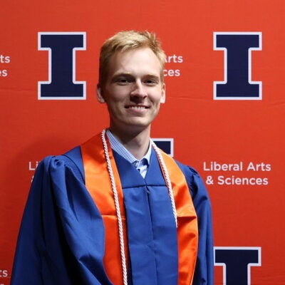 Jacob Strand in graduation regalia in front of an orange LAS backdrop