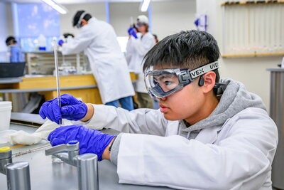 Student in lab wearing goggles, gloves and a lab coat doing chemistry