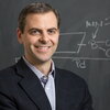 Head shot of Martin Burke in a suit jacket and collared shirt in front of a blackboard with chemistry calculations