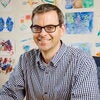 Portrait of Martin Burke seated with a white wall behind him that is full of colorful drawings