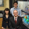 Three researchers stand side by side near equipment in a chemistry lab.